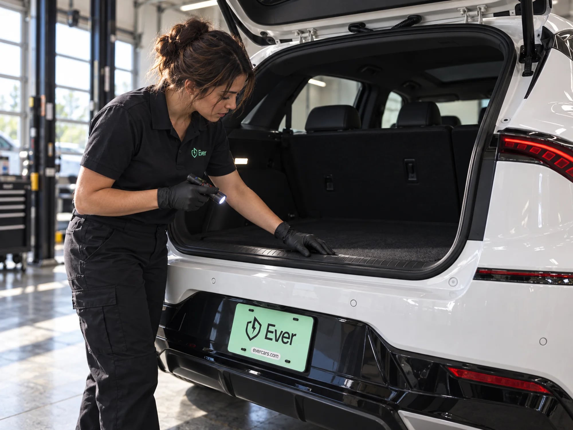 An Ever technician checks the open trunk of a white EV with a flashlight